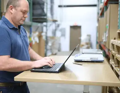 stock control operative working at laptop in warehouse